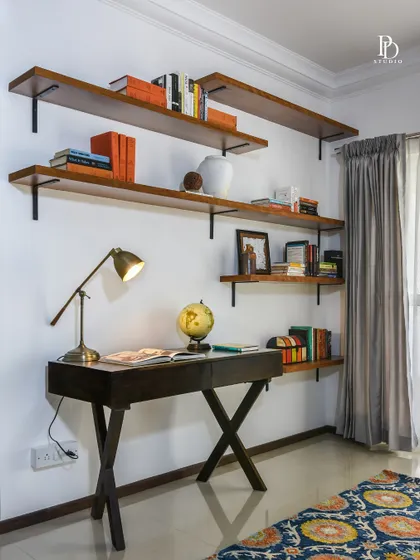 This simple yet elegant study corner features floating wooden shelves for books and decor. The minimalist desk and warm lighting create a functional and inspiring workspace within the main living area.