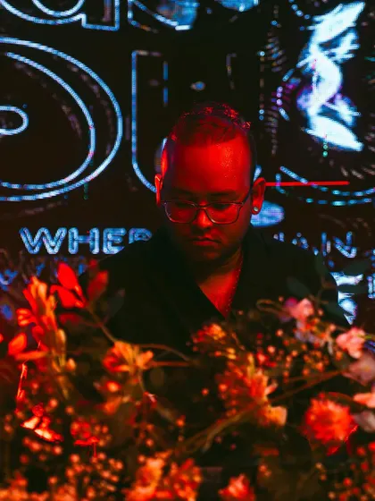 A close-up during my set, bathed in the red and blue light of the 'Masala House' visuals. I focus on weaving a seamless journey through different Indian-inspired electronic tracks.