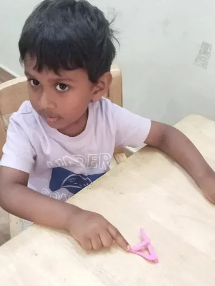 A young boy points to the letter 'A' he has formed out of pink clay. This is a fun, hands-on way to practice letter recognition and formation.