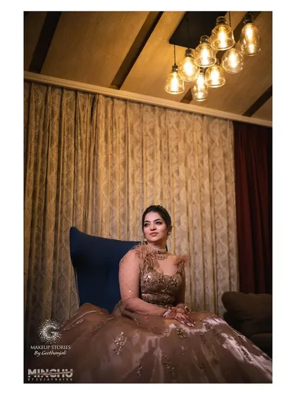 A wide shot of Reshma seated for her cocktail party. The makeup is designed to look stunning in low light, with a focus on luminous skin and dramatic eyes.