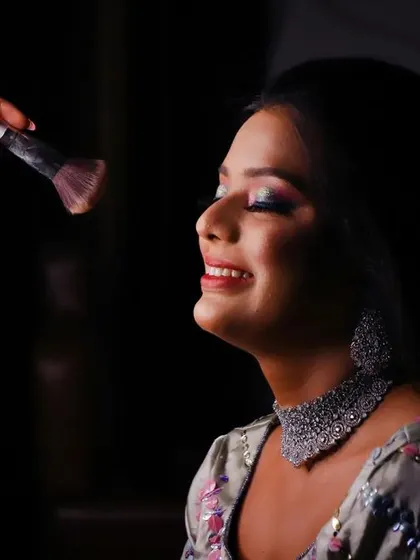 A close-up of the bride getting her makeup done. This candid shot captures her happy smile and the final touches before her big moment, highlighting the anticipation.