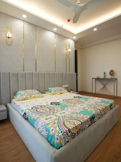 This bedroom features a grey velvet-upholstered bedframe paired with a stunning panel wall enhanced by vertical gold trims and warm wooden flooring.