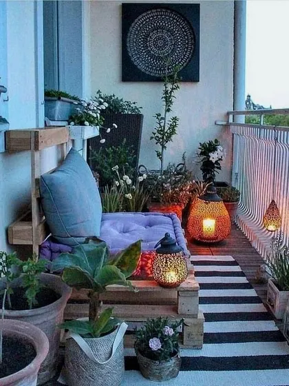 An inspirational image showing a cozy balcony setup with pallet furniture, lanterns, and an abundance of potted plants, demonstrating how to create a bohemian-style retreat in a small space.