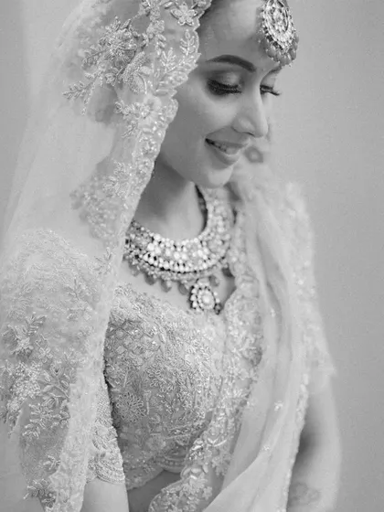 A delicate black and white close-up of the bride, capturing her happy expression and the intricate details of her embroidered veil.