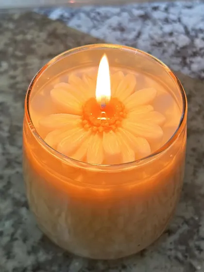 A lit daisy candle, showing how the wax flower melts beautifully into the candle pool.