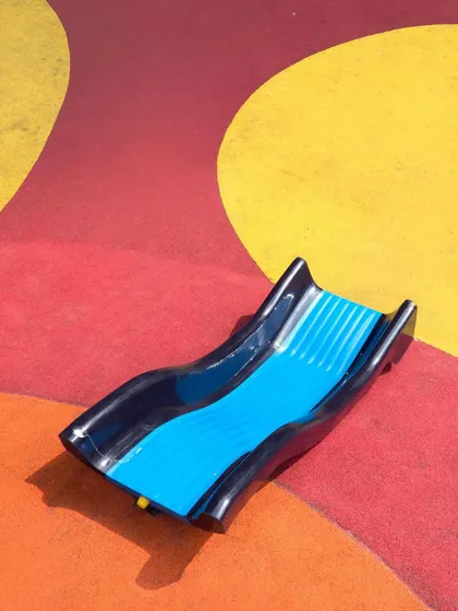 A detail of the slide integrated into the colorful, undulating EPDM flooring of the play area, creating a seamless and playful landscape.
