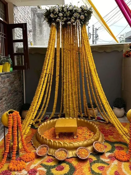 A beautiful Haldi seating arrangement created on a home terrace. We used a canopy of marigold strings, traditional matkas, and a large urli to transform the space into a perfect ceremony spot.