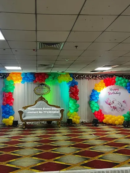 A colorful birthday stage featuring a rainbow balloon ring and a matching balloon arch. The white sofa in the middle is perfect for seating the birthday person for photos.