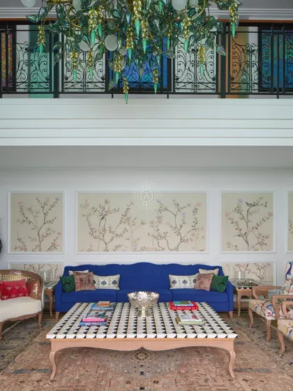 The main seating area is set against a wall with delicate, hand-painted wallpaper panels. The deep blue sofa provides a strong color anchor in the otherwise light and airy space.