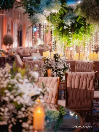 A close-up of the reception seating, showing the elegant blush-toned chairs and tables adorned with baby's breath. The soft lighting and abundant florals create a romantic and sophisticated ambiance.