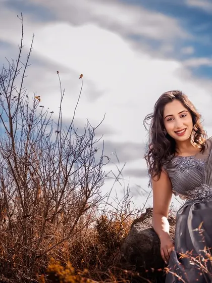A beautiful solo portrait of the woman in her elegant grey gown, seated on a rock with the bright blue sky and clouds creating a stunning backdrop.
