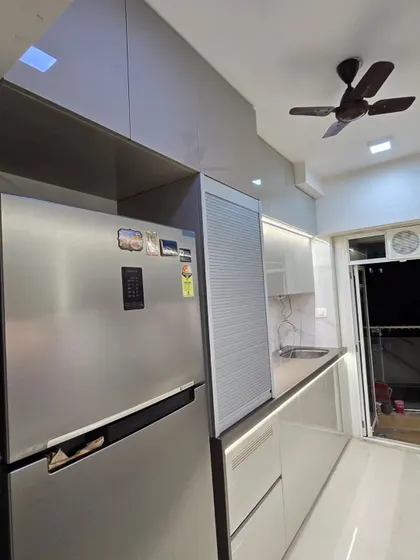 This kitchen integrates a refrigerator seamlessly next to a roller shutter unit for small appliances. The glossy, light-colored cabinets and handleless design contribute to a clean and modern look.