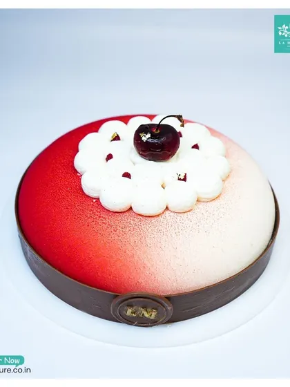 This is my Black Forest Revisited cake. It features a modern design with a red and white velvet spray finish, a chocolate collar, and a single fresh cherry on top of delicate cream piping.