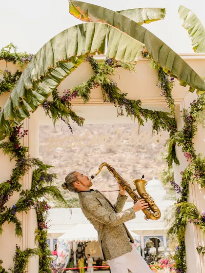 Live entertainment is key to a lively event. Here, a saxophonist serenades guests under an arch of banana leaves and florals, adding a touch of class and creating a wonderful ambiance.