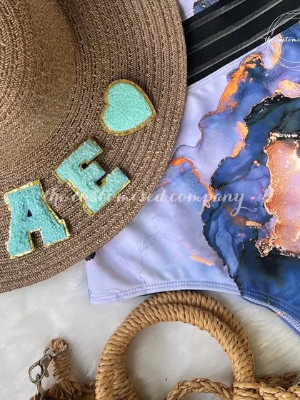 Just what you need for your summer vacay. This flat-lay shows a custom "BAE" sun hat, a stylish swimsuit, and a straw bag, creating the perfect beach-ready look.