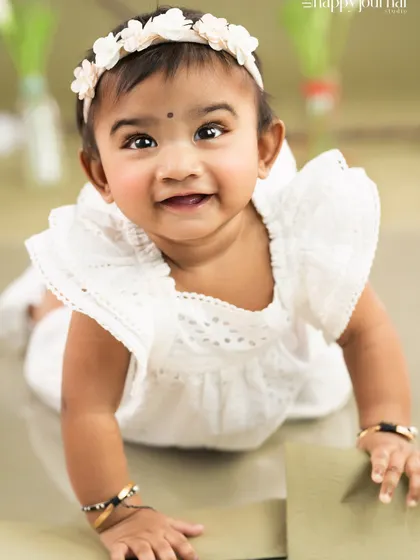 A happy baby girl crawling on the floor, looking right at the camera with a big, heartwarming smile.