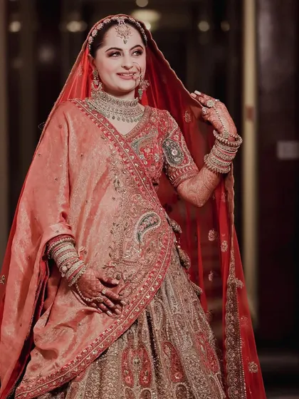 A full-length portrait of the bride in her beautiful peach and red lehenga, looking radiant and ready for her big day.