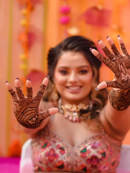 The bride happily shows off her elaborate Mehendi design. The focus is on the detailed henna art covering her hands and arms.