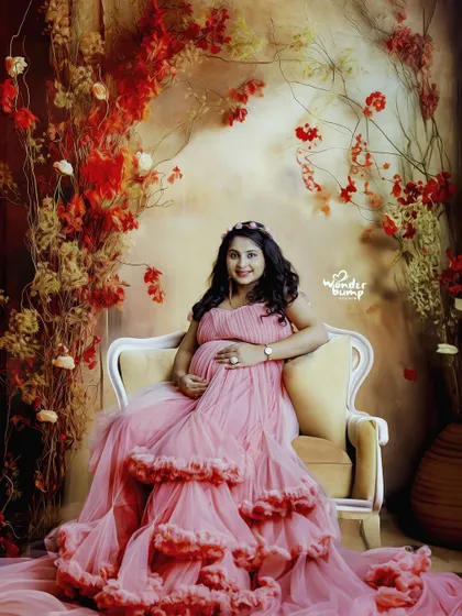 A regal portrait in a pink ruffled gown, seated on an elegant chair against a warm, floral-themed backdrop.