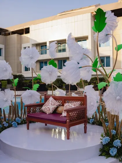 A whimsical photo booth with a dark wood bench set against a backdrop of oversized white paper flowers, creating a fairytale-like spot for pictures.