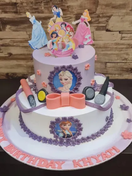 A two-tier cake fit for royalty, combining the worlds of Disney Princesses and Frozen. The design includes character images and edible makeup accessories for a magical theme.