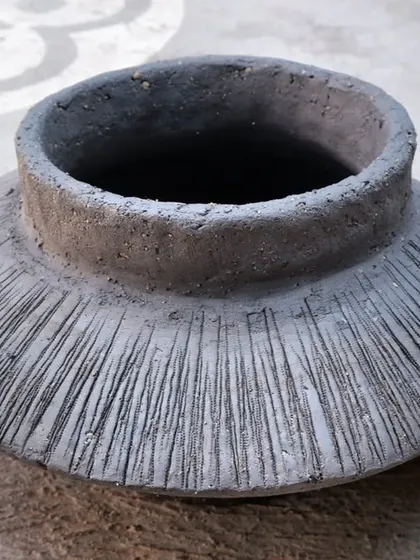 A textured pot after Raku firing. The unglazed clay body has absorbed the smoke, turning it a deep, matte black, while the carved lines add a beautiful tactile quality.