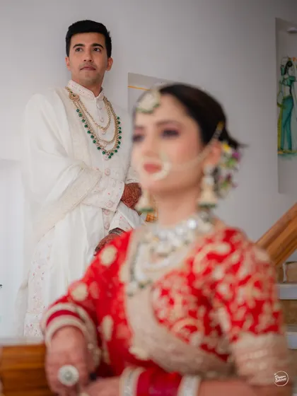 An artistic shot with the groom in focus and the bride softly blurred in the foreground, creating a sense of depth and anticipation.