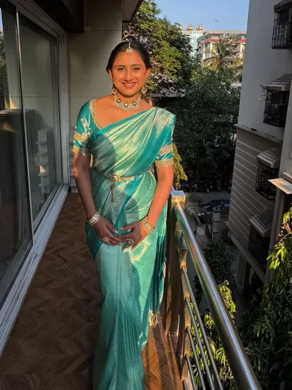 A full-length shot of the sister in the teal saree. The pleats are perfectly aligned, and the pallu is draped to create a graceful and flattering silhouette, perfect for a wedding guest.