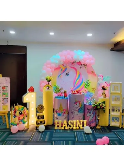 A whimsical unicorn-themed first birthday for Hasini. This decor includes a large unicorn backdrop, a milestone board showing her first year, and soft pastel colors throughout.