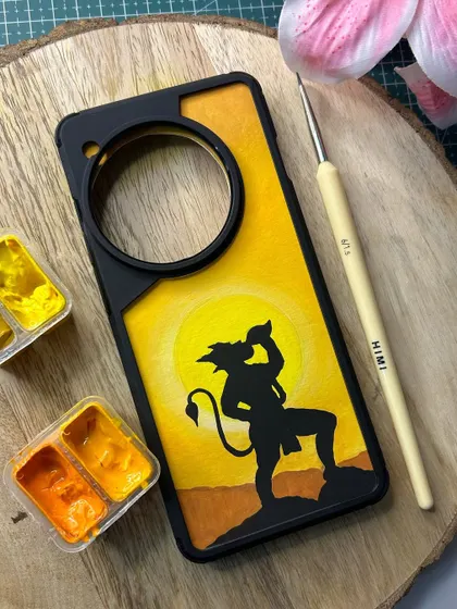 A powerful silhouette of Hanuman ji carrying the Sanjeevani mountain, painted on a custom phone cover. The warm sunset colors create a dramatic and inspiring background.