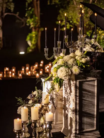 An elegant candelabra with black taper candles stands beside a lush floral arrangement, creating a moment of sophisticated drama. The composition is a testament to our belief that beauty lies in the details.