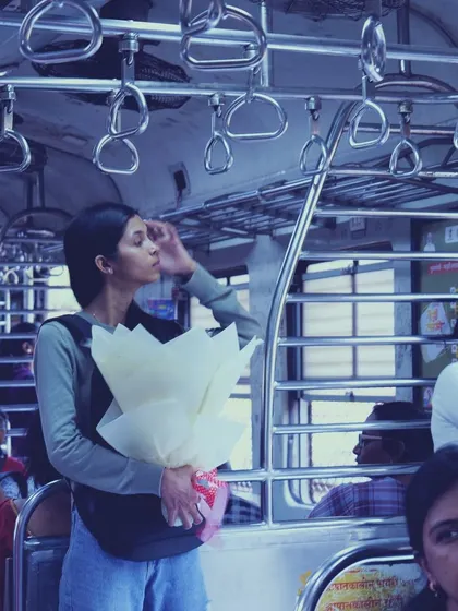 Another commuter in the Mumbai local, holding a bouquet of white flowers. This candid shot captures her standing journey, a common sight in the city's lifeline.