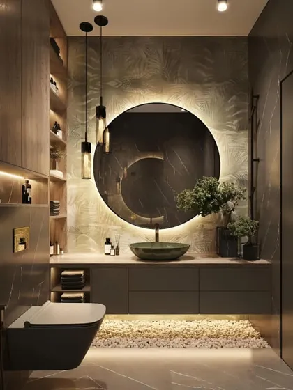 I create bathrooms that feel like a personal spa. This design features a bold, back-lit circular mirror, a vessel sink, and a mix of dark tiles and textured wallpaper to create a moody and sophisticated atmosphere with plenty of smart storage.