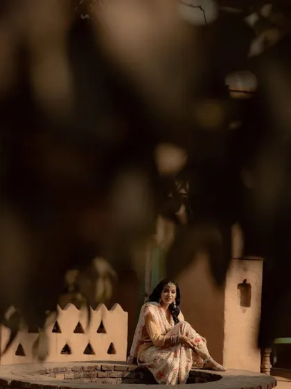 A beautifully framed portrait of the bride sitting by a traditional well, using natural foliage to create a sense of intimacy and mystery.