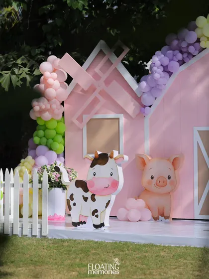 A closer look at the main barnyard backdrop. Our custom-made cow and pig characters stand cheerfully in front of the pink barn, surrounded by pastel balloon garlands, making for a perfect birthday photo spot.