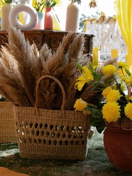 Details of a boho-chic Haldi setup, featuring pampas grass and yellow flowers in woven baskets.