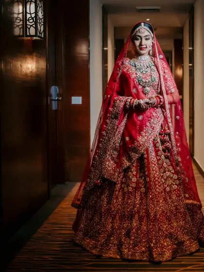A full-length portrait of the bride in a hotel corridor. The leading lines of the hallway draw attention to her and her magnificent red lehenga.