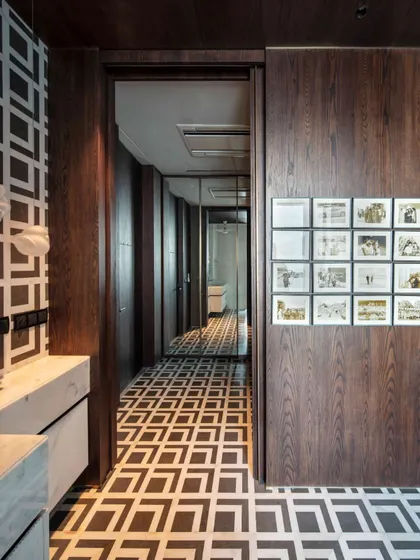 The master washroom is a study in monochrome elegance, with a striking geometric pattern of Indian white and grey marble on the floor and wall. A sliding door reveals a gallery wall of cherished family photos.