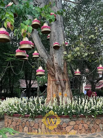Brass bells adorned with pink flowers hanging from a tree. This beautiful detail added to the serene and traditional ambiance of the wedding venue.