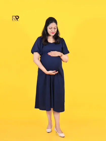 A classic solo maternity pose. The mom-to-be cradles her bump, her simple navy dress and the bright yellow background creating a cheerful and timeless image.