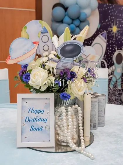 A beautiful table centerpiece combining fresh white roses with space-themed cutouts, blending elegance with fun.