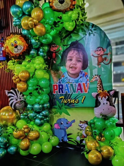 A personalized jungle theme welcome sign for a first birthday party. This setup features a custom poster with the child's photo, surrounded by a green and gold balloon arrangement with animal foil balloons.