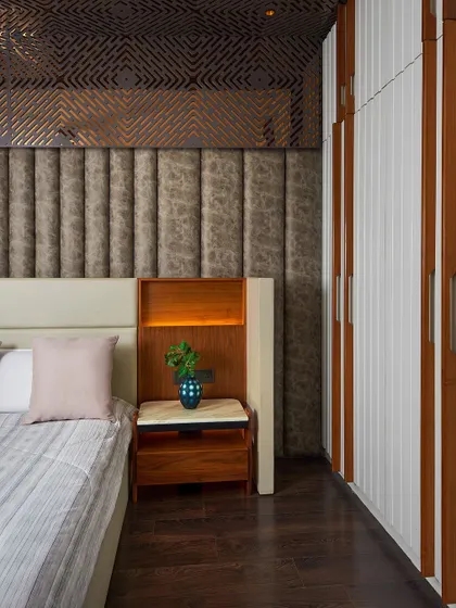 A close-up of the bedside area, showing the rich combination of a tufted fabric headboard, a custom wooden side table with a marble top, and a decorative screen that adds a layer of intricacy to the ceiling.
