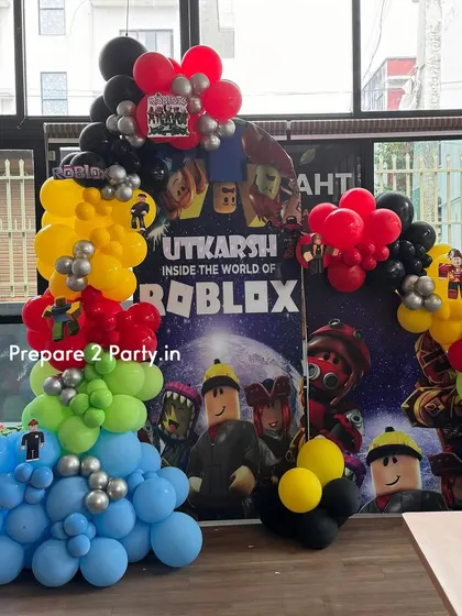 Enter the world of Roblox with this gaming-themed birthday decoration. The setup includes a large, printed backdrop of the game world and a colorful balloon arch that mimics the blocky aesthetic.