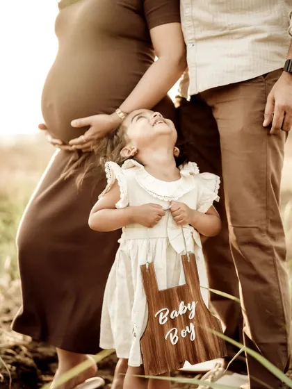 A heartwarming gender reveal. The older sister looks up at her parents, holding a sign that says "Baby Boy," announcing the new addition to the family.