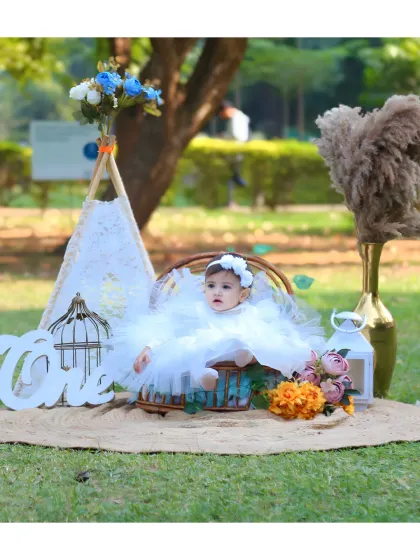 A beautiful outdoor first birthday setup with a teepee and 'One' sign for a baby girl in a white dress.