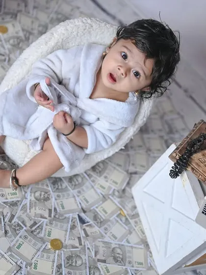 A wider shot of the 'Money' theme, showing the baby surrounded by prop currency and a vintage telephone.