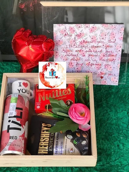 A romantic wooden tray hamper for Valentine's Day. It includes a "I love you" shot glass, chocolates, a mini heart balloon, and a handwritten note.