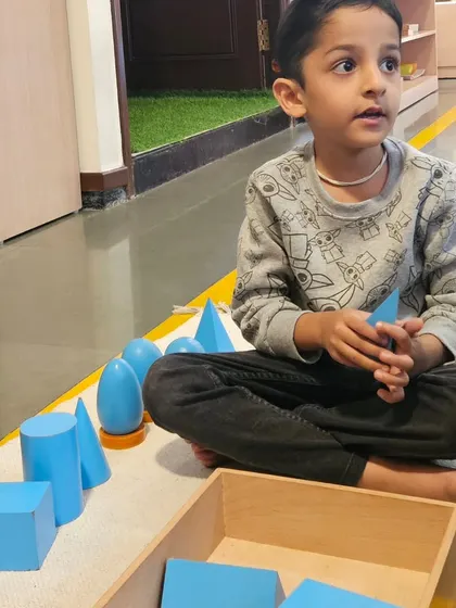 Exploring geometric solids helps children understand three dimensional shapes in their environment. This sensorial work allows them to distinguish different forms like cubes, spheres, and cones by touch and sight, building a vocabulary for the world around them.