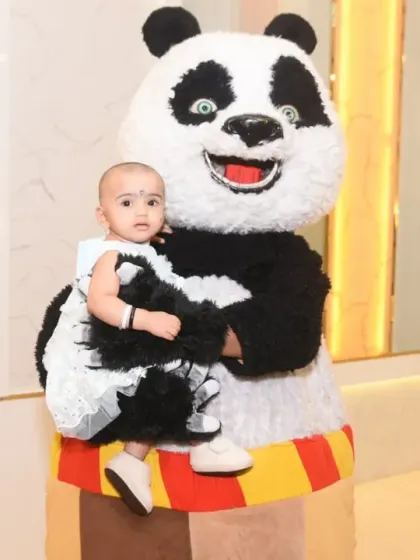 A cute and funny moment as a baby dressed in a panda-like outfit is held by a panda mascot.